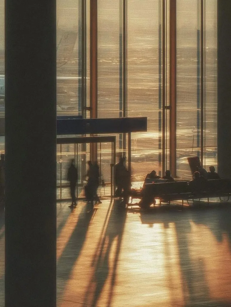 travellers silhouetted against an airport terminal window at sunrise